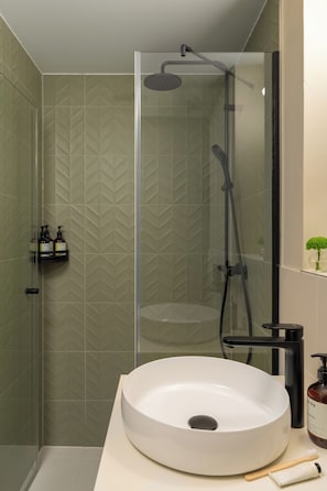 Un baño moderno con ducha envuelta en vidrio, un lavamanos blanco tipo recipiente y artículos de tocador sobre la encimera.