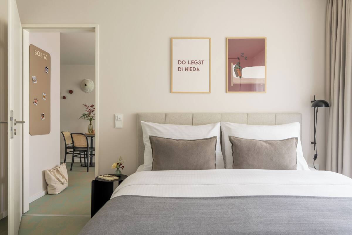 A bedroom with a bed, bedside table, lamp, and wall art.