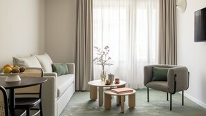 Een moderne woonkamer met een bank, fauteuil, een rond salontafeltje en een klein bijzettafeltje met een vaas en boeken.