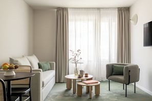 Un salon moderne comprenant un canapé, un fauteuil, une table basse ronde et une petite table d’appoint avec un vase et des livres.