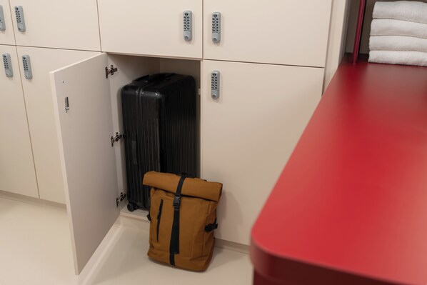 Una habitación con un mostrador rojo, una maleta marrón y una maleta negra debajo de un armario con múltiples cerraduras.