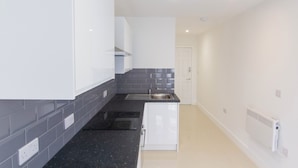A modern kitchen with white cabinets, a black countertop, a stainless steel sink, and a built-in oven. - Bridge Road - Room 1 (Southampton)