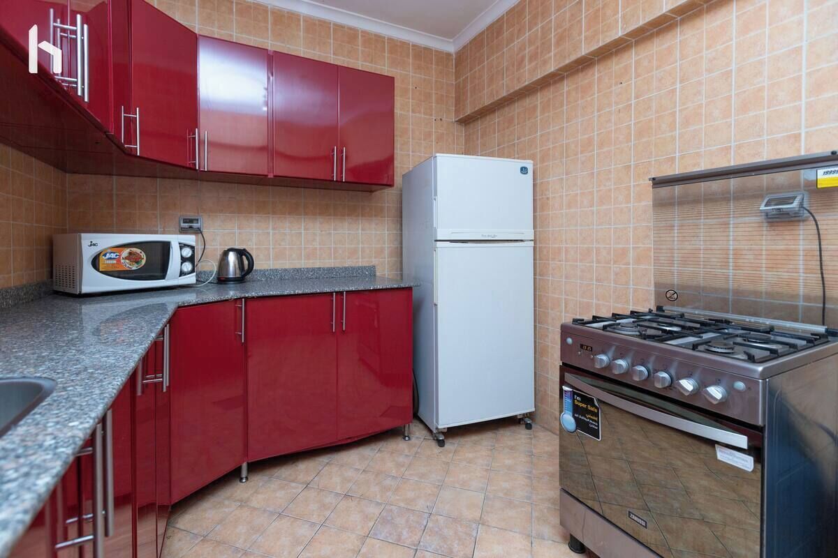 A compact kitchen with red cabinets, a white refrigerator, a microwave, a stove, and a coffee maker.