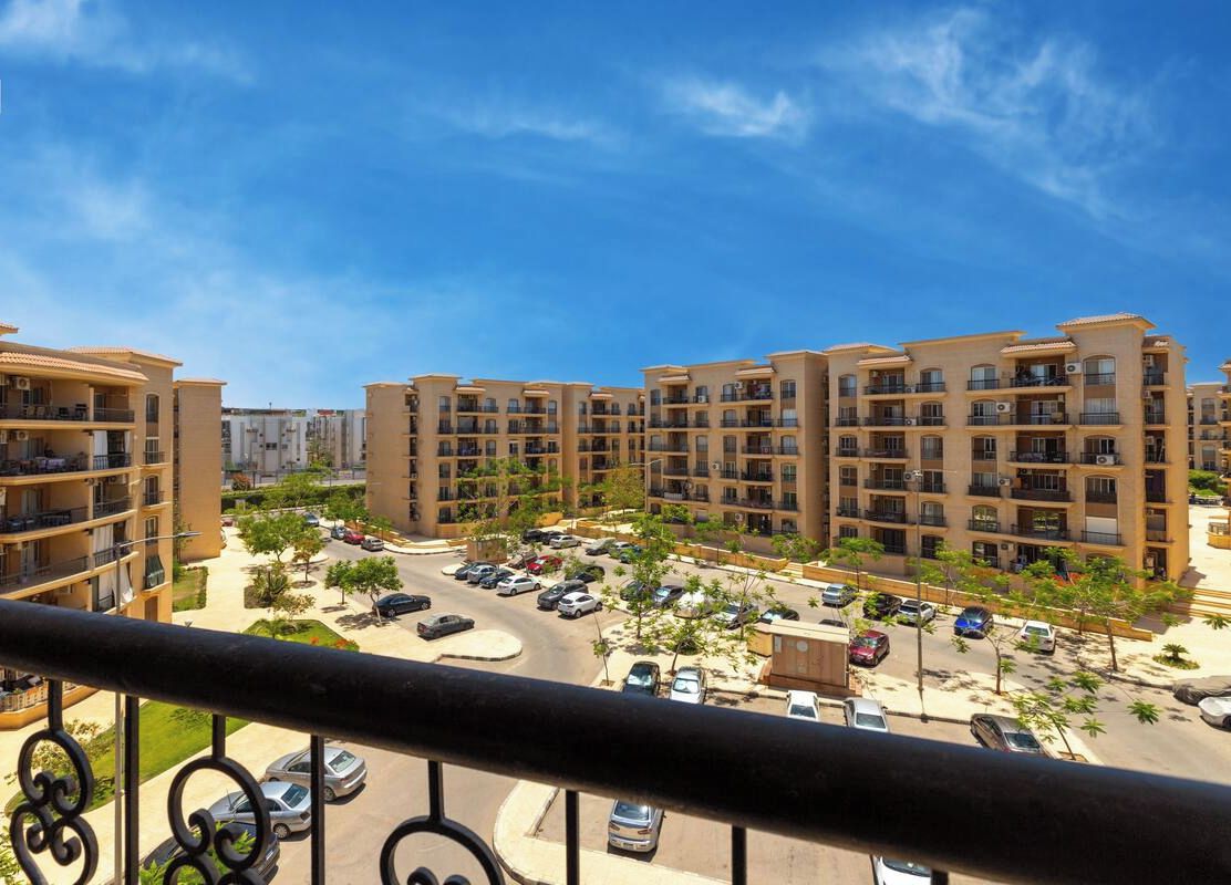 Un edificio residencial con varios balcones, un estacionamiento y un cielo azul despejado.