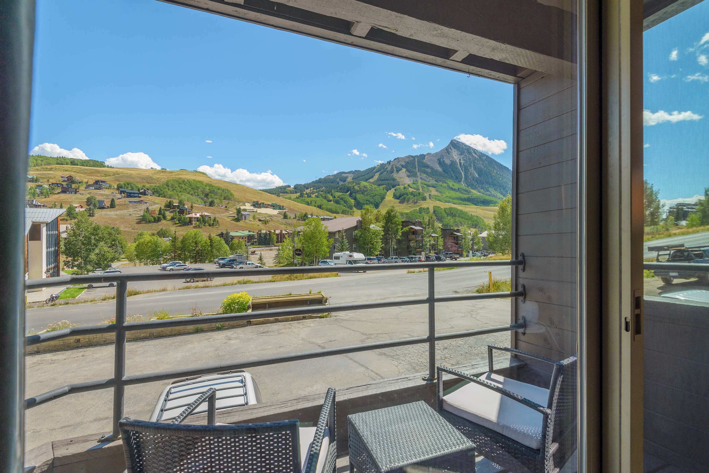 A balcony with a view of a mountainous landscape, a parking area, and a building with a flat roof.