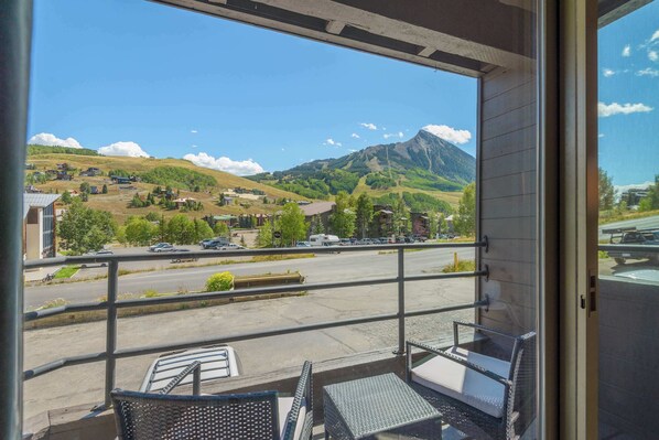 A balcony with a view of a mountainous landscape, a parking area, and a building with a flat roof.