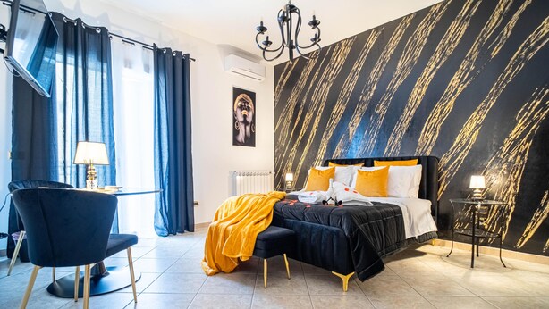 A bedroom with a bed, a chair, a table, and a wall with a unique pattern. - Suite del Corso (Ficarazzi)
