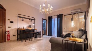 A modern living room with a sofa, a dining area with chairs, a chandelier, and a view of the outdoors. - Suite del Corso (Ficarazzi)