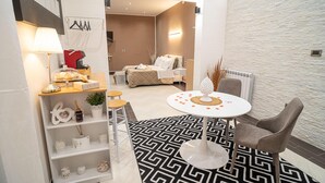 A modern hotel room with a bed, a round table with a decorative centerpiece, a small seating area with stools, and a white patterned rug. - Suite del Corso (Ficarazzi)