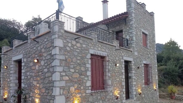 Un edificio de piedra con balcón, plantas en macetas e iluminación exterior.