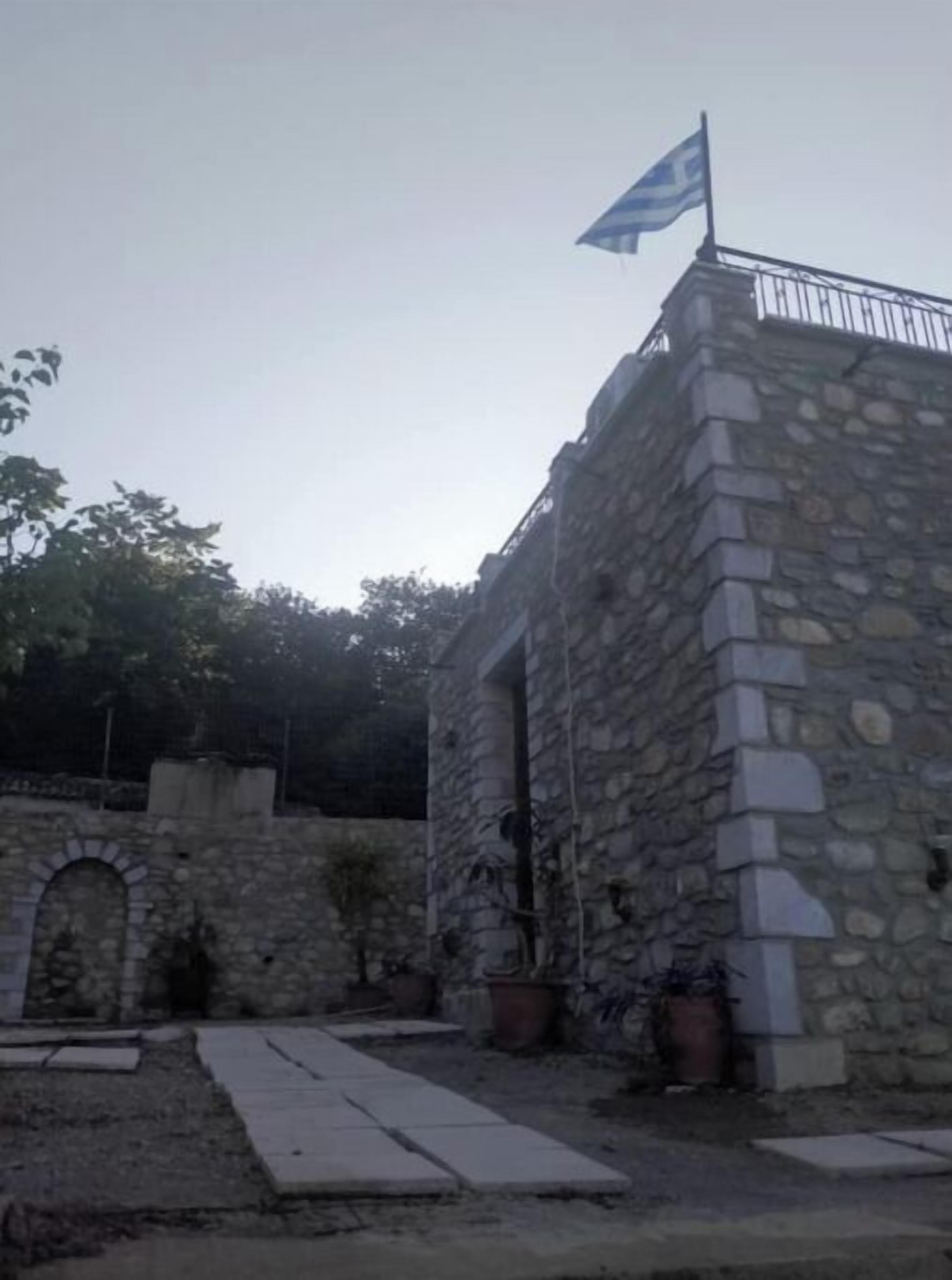 A stone building with a flag on top, a stone archway, and potted plants.