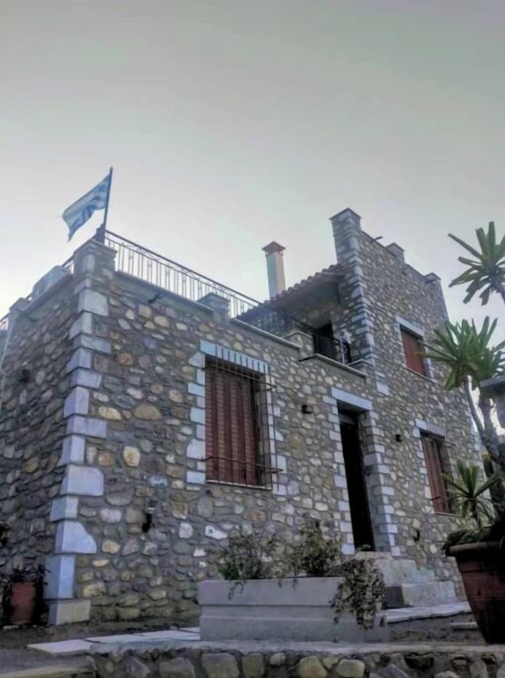 Um edifício de pedra com bandeira, chaminé e varanda.