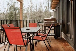 Une terrasse extérieure avec une table en bois et des chaises rouges, un barbecue et une vue sur les arbres.