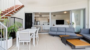 Un apartamento moderno con comedor, sala de estar con sofá y televisor, y cocina al fondo.
