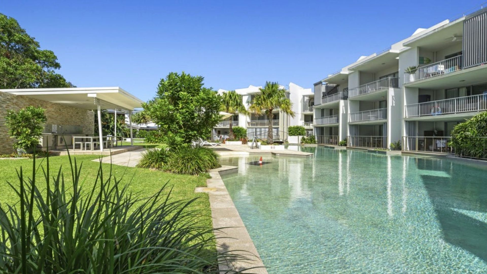 A modern hotel with a swimming pool, outdoor seating, and lush greenery.