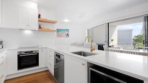 Cocina moderna con armarios blancos, horno empotrado y lavavajillas. Amplia ventana con vistas al exterior.