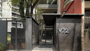 Entrada murada com portão de metal e muro de concreto exibindo o número 'V72'.