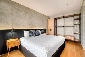 A modern bedroom with a large bed, wooden nightstands, a built-in wardrobe, and a shelf unit.