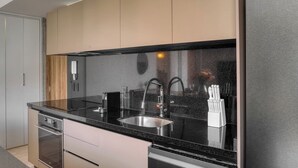 Cozinha moderna com pia de aço inoxidável, bancada preta e armários de madeira.