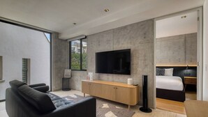 Quarto moderno com cama grande, TV na parede e sofá na sala.