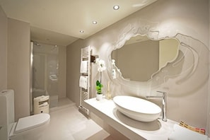 A modern bathroom with a large mirror, a white sink, and a shower area. - Truly Verona (Verona)