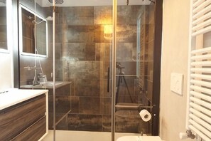 A bathroom with a glass-enclosed shower, a mirror, and a white sink.