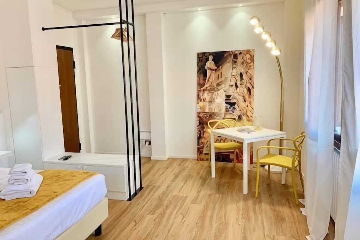 A hotel room with a bed, bedside table, lamp, and a small table with chairs.