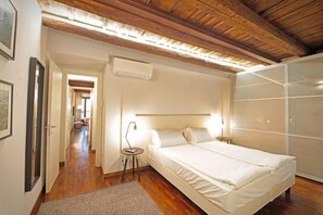 Ein Schlafzimmer mit einem Bett, Nachttischen, einem Holzfußboden und einem Flur, der in ein weiteres Zimmer führt.