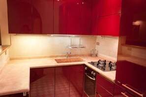 A compact kitchen with red cabinets, a countertop, and a gas stove. - Truly Verona (Verona)