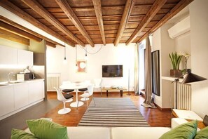 A modern kitchen with white cabinets, a dining area with a white table and chairs, a sofa with green cushions, and a wooden ceiling. - Truly Verona (Verona)