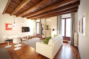 A modern living room with a white sofa, a dining table, and a TV. - Truly Verona (Verona)
