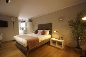 A bedroom with a bed, bedside table, lamp, and a potted plant. - Truly Verona (Verona)