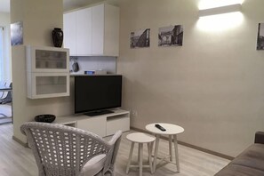 A modern living room with a flat-screen TV, a wicker chair, two small tables, and a sofa. - Truly Verona (Verona)