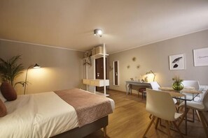A bedroom with a bed, bedside table, lamp, desk, chair, and a small balcony.