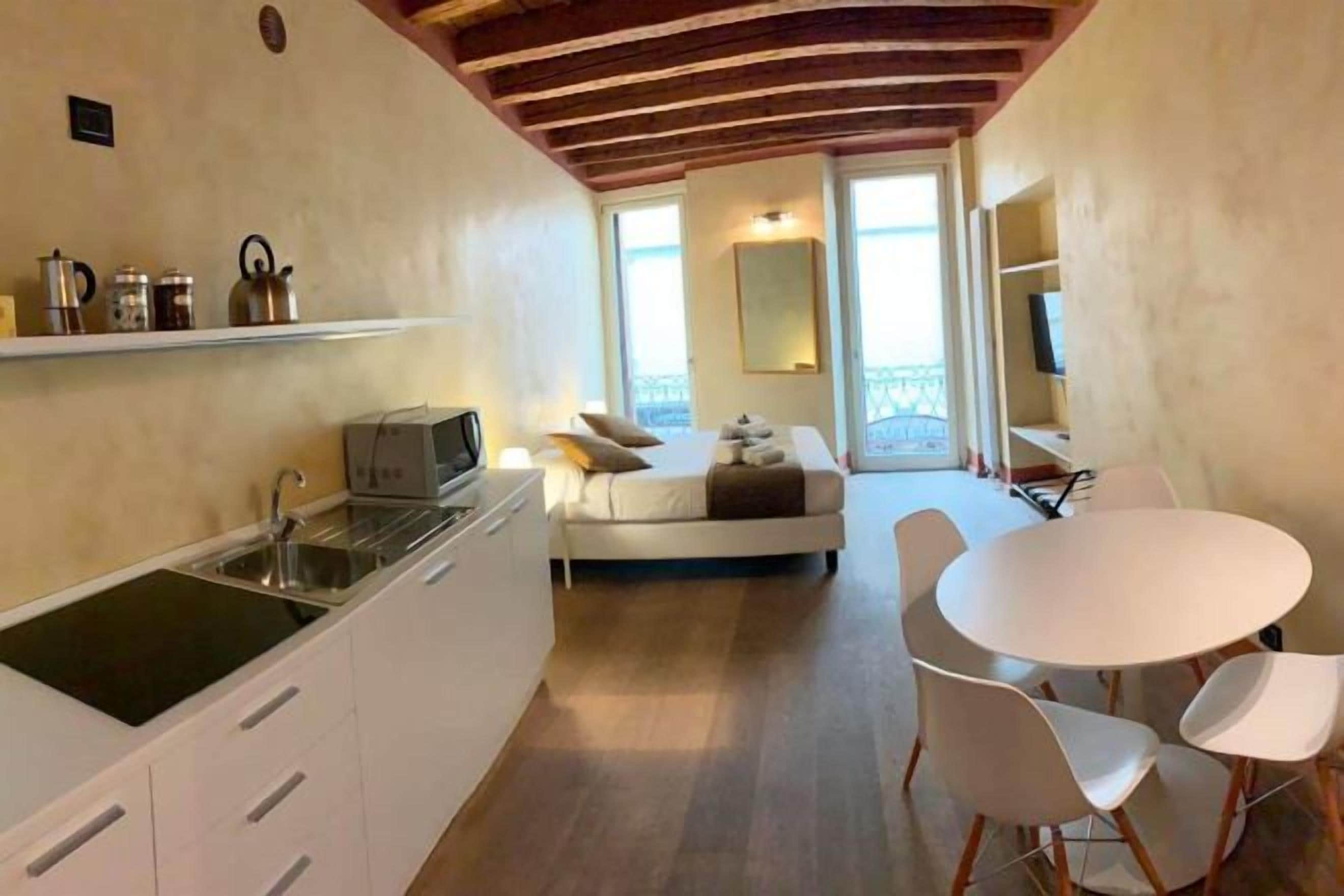 A compact kitchen with a microwave, sink, and cabinets, a dining area with a round table and chairs, and a balcony with a sofa.