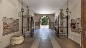 A corridor with a tiled floor, two metal gates, a large arched doorway, and a bicycle parked by the gates. - Truly Verona (Verona)