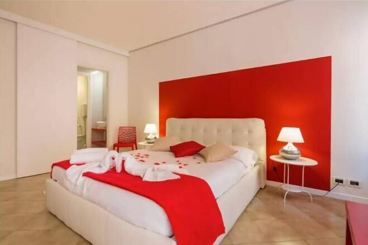 A modern bedroom with a large bed, red accent wall, and two bedside lamps.