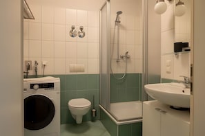 Une salle de bain équipée d’un lave-linge, de toilettes, d’une douche et d’un lavabo.