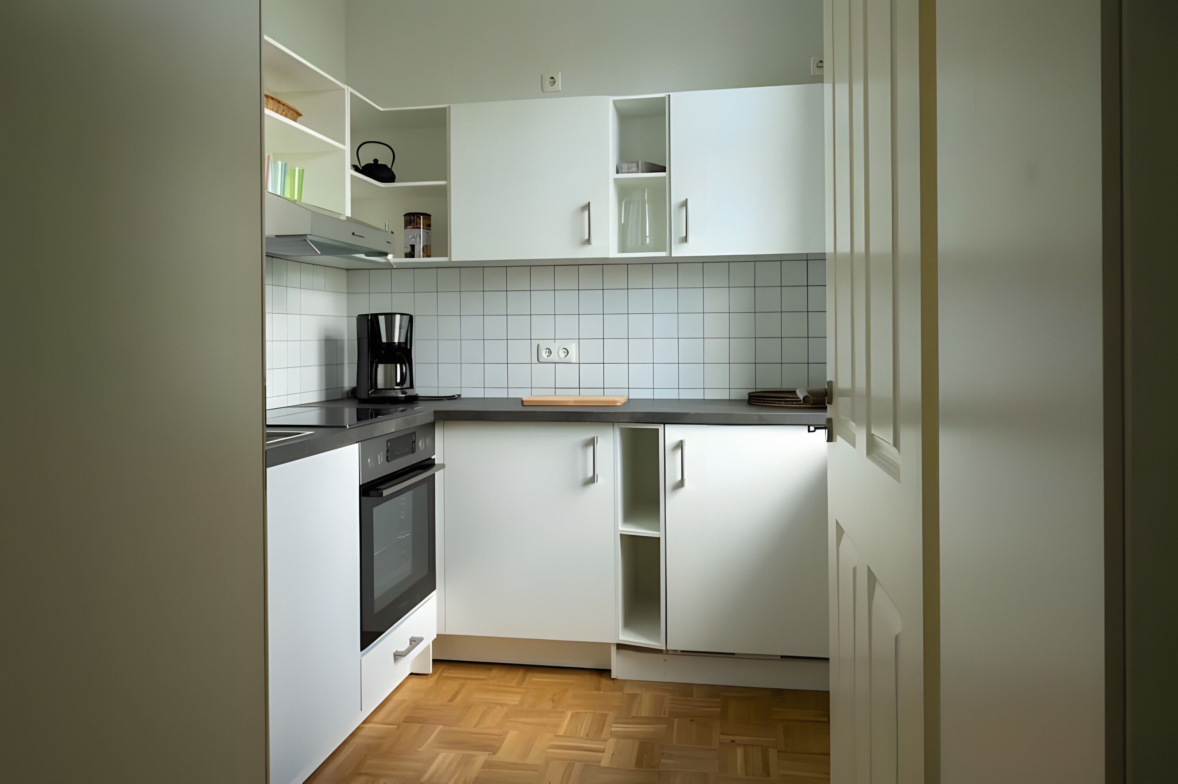Une cuisine moderne avec des meubles blancs, un plan de travail noir et un plancher en bois.