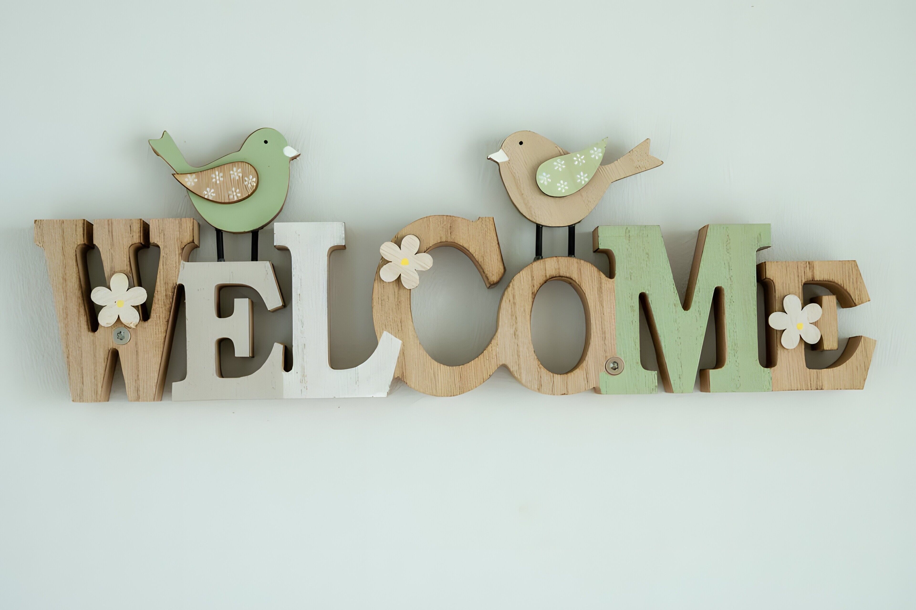 Et træskilt med ordet 'WELCOME' og to fugle siddende på det.