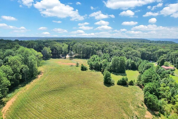 Une vue aérienne d’un paysage rural, avec un vaste champ ouvert, une forêt dense et un petit bâtiment.