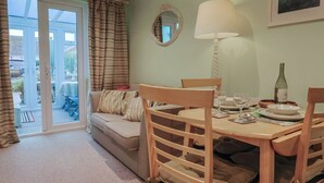 A dining area with a table set for four, a sofa, and a window with curtains. - Cherry Pip (Bridport)