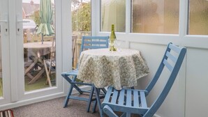 A small room with a table and chairs, a bottle of wine, and a view through a glass door. - Cherry Pip (Bridport)