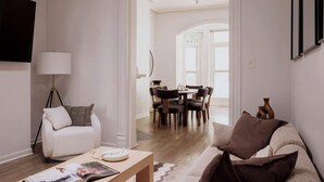 A modern living room with a sofa, a coffee table with a magazine, a lamp, and a TV on the wall. - Designer Combo Loft 2E & 2W|Gold Coast/River North (Chicago)