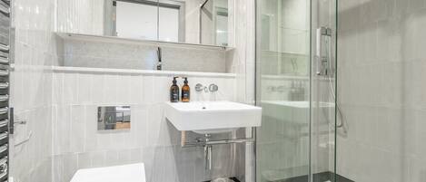 A modern bathroom with a glass shower enclosure, a white sink, and a toilet.