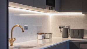 Una cocina moderna con encimera de mármol, un grifo dorado, un tostador GINO y una tetera.