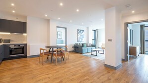 Una cocina moderna con electrodomésticos integrados, un comedor con sillas de madera, una sala de estar con sofá y una mesa de centro, y un pasillo que conduce a otra habitación.