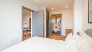 Un dormitorio moderno con una cama grande, una puerta de madera que da a un baño y una pequeña mesa con sillas.