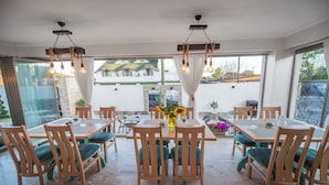 A dining area with wooden tables and chairs, a chandelier, and large windows with curtains. - Thaya Rooms (Mangalia)