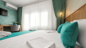 A hotel room with a bed, a desk, a chair, a TV, and a window with curtains. - Thaya Rooms (Mangalia)